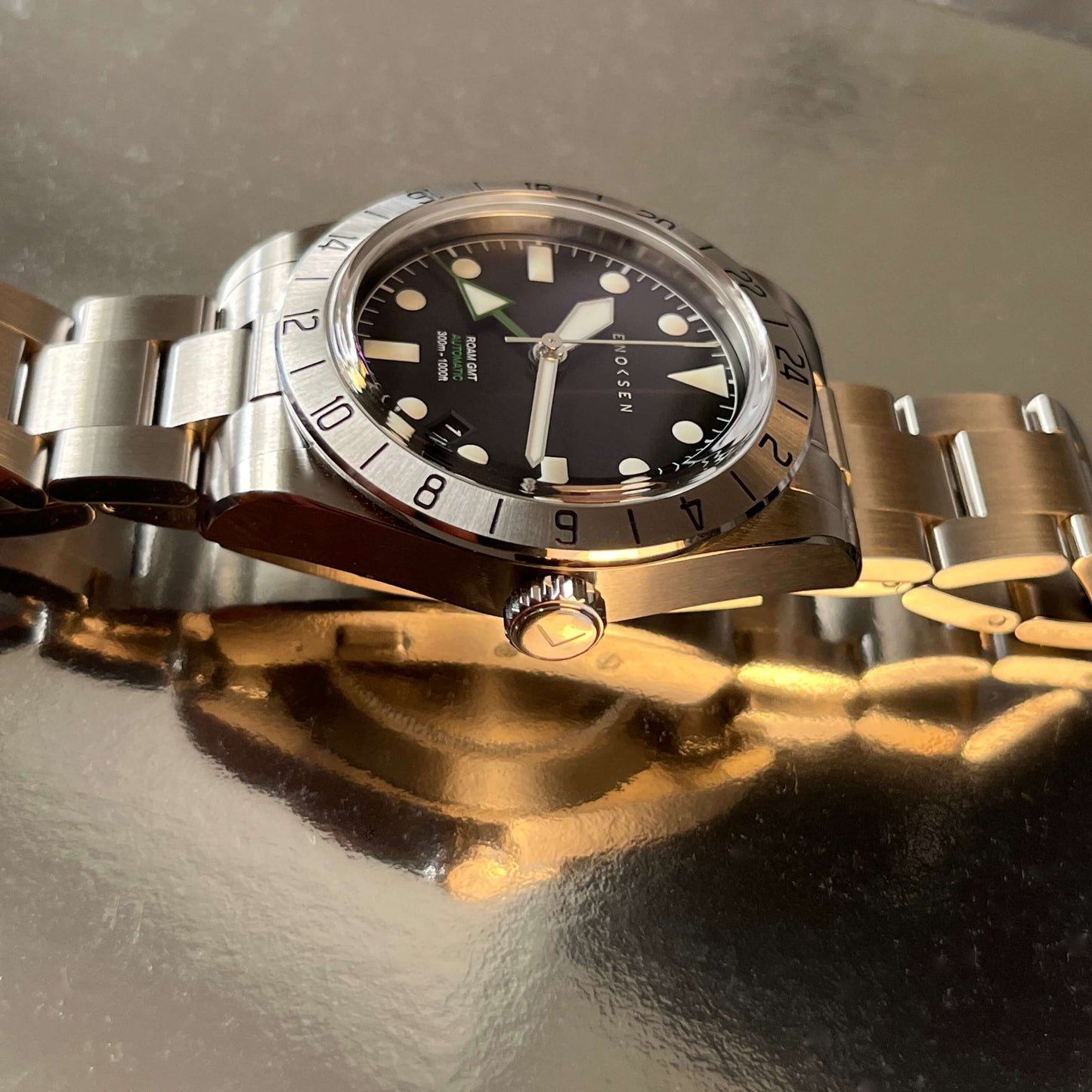 A side-on view showcasing the polished steel case of By Enoksen GMT watch. The image emphasizes the watch's elegant slim profile, and the crystal-clear durable sapphire crystal.