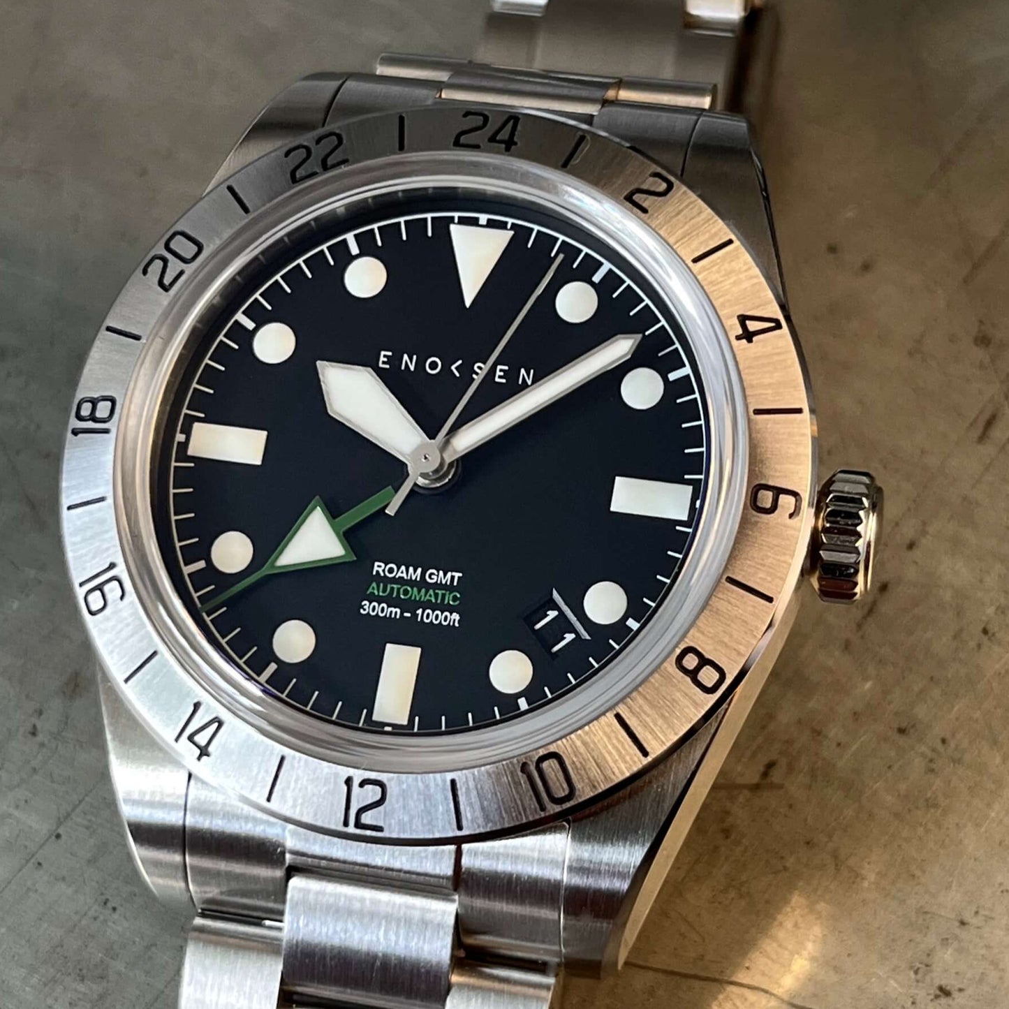 Close up of dial, showing the crisp hour, minute and seconds hands, as well as the Enoksen green 24-hour GMT hand and rotating bezel.