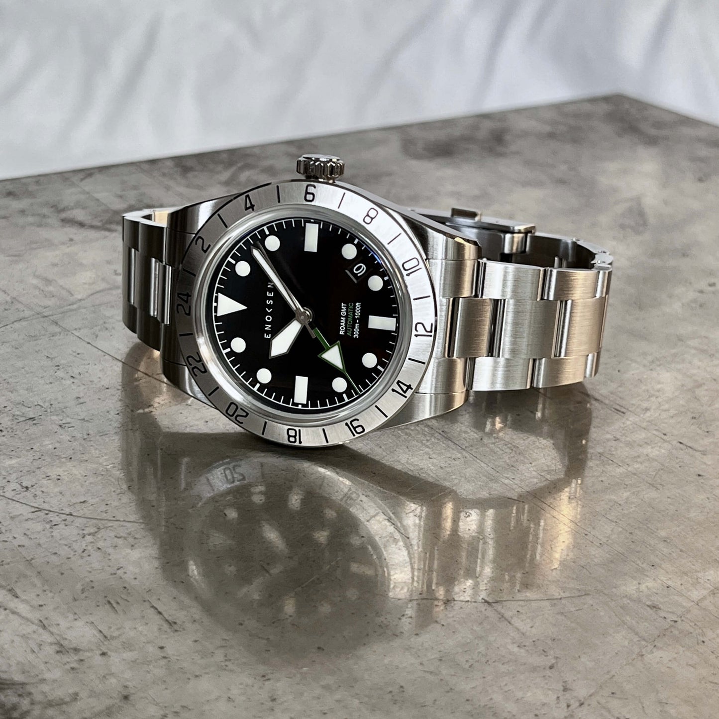 Roam E07/B men's automatic GMT By Enoksen watch featuring a polished stainless steel link bracelet, front view. The image emphasizes the anti-reflective, scratch-resistant sapphire Crystal.