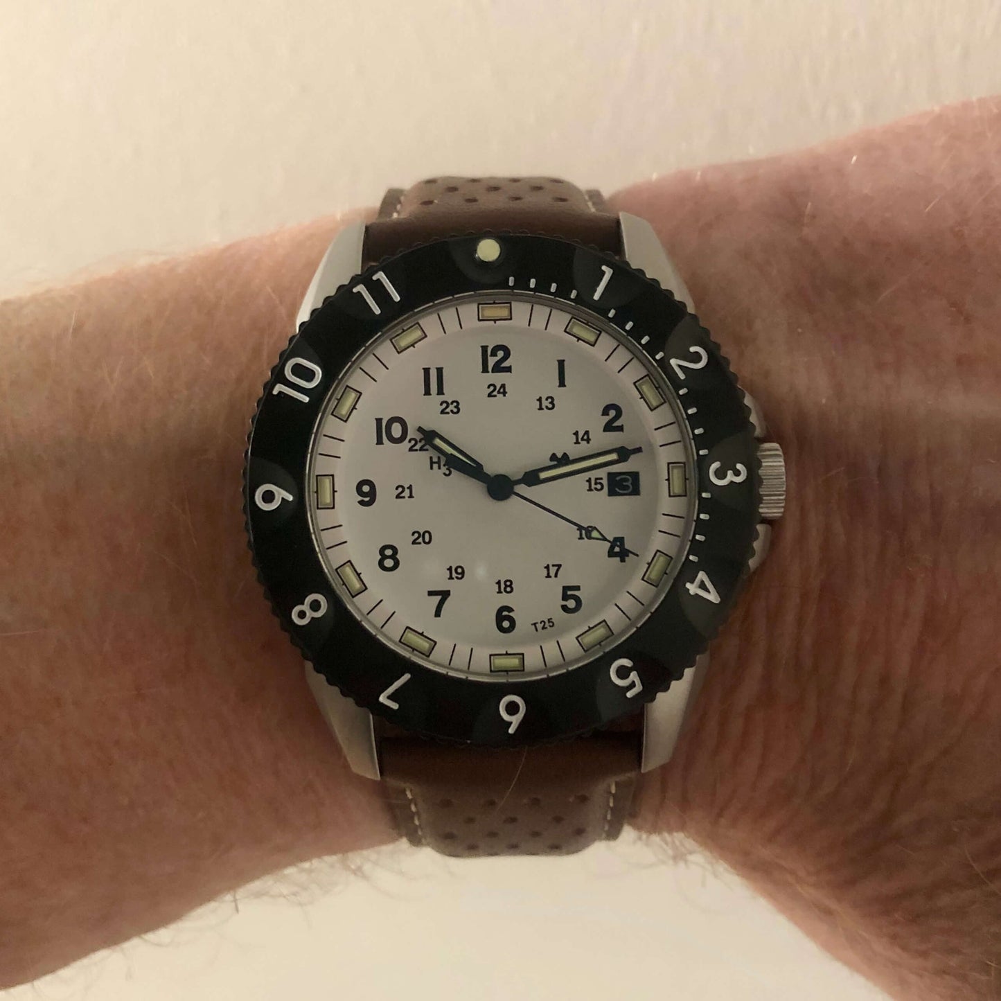 Close up of Tactical watch featuring the white dial of model E09A. Watch seen on a wrist with a brown leather strap.