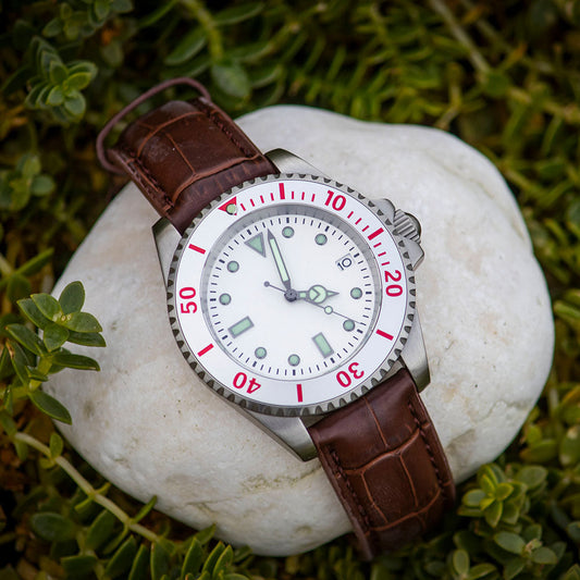Watch with brown leather strap on a white stone surrounded by green grass
