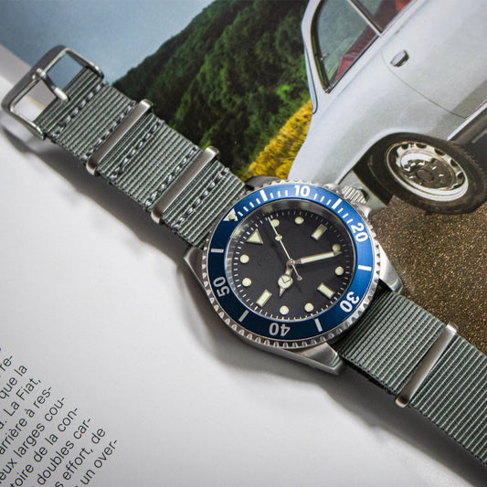 Watch with a blue bezel on a surface with a blurred car and landscape in the background