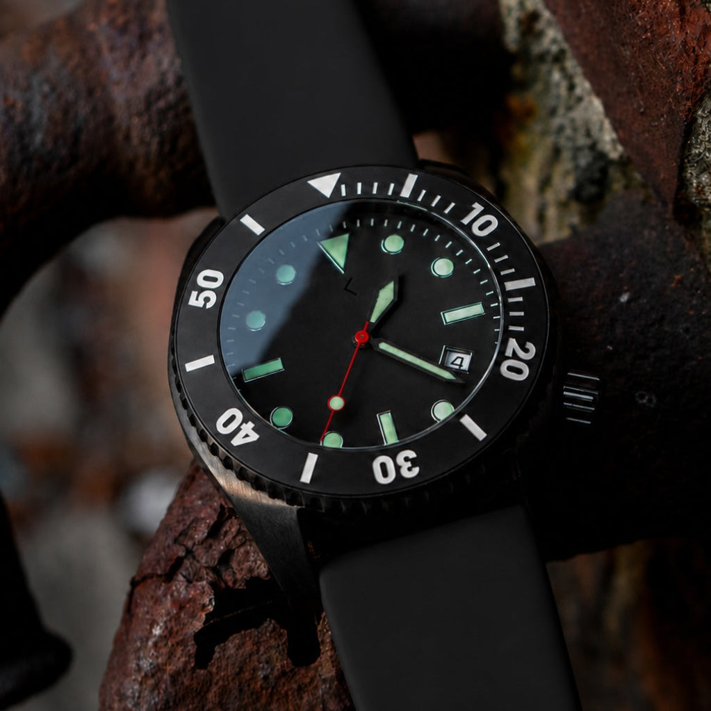 A black analog dive watch with a matte black strap, black bezel, and luminous green and white details, resting on a rusty metal structure.