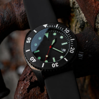 A black analog dive watch with a matte black strap, black bezel, and luminous green and white details, resting on a rusty metal structure.