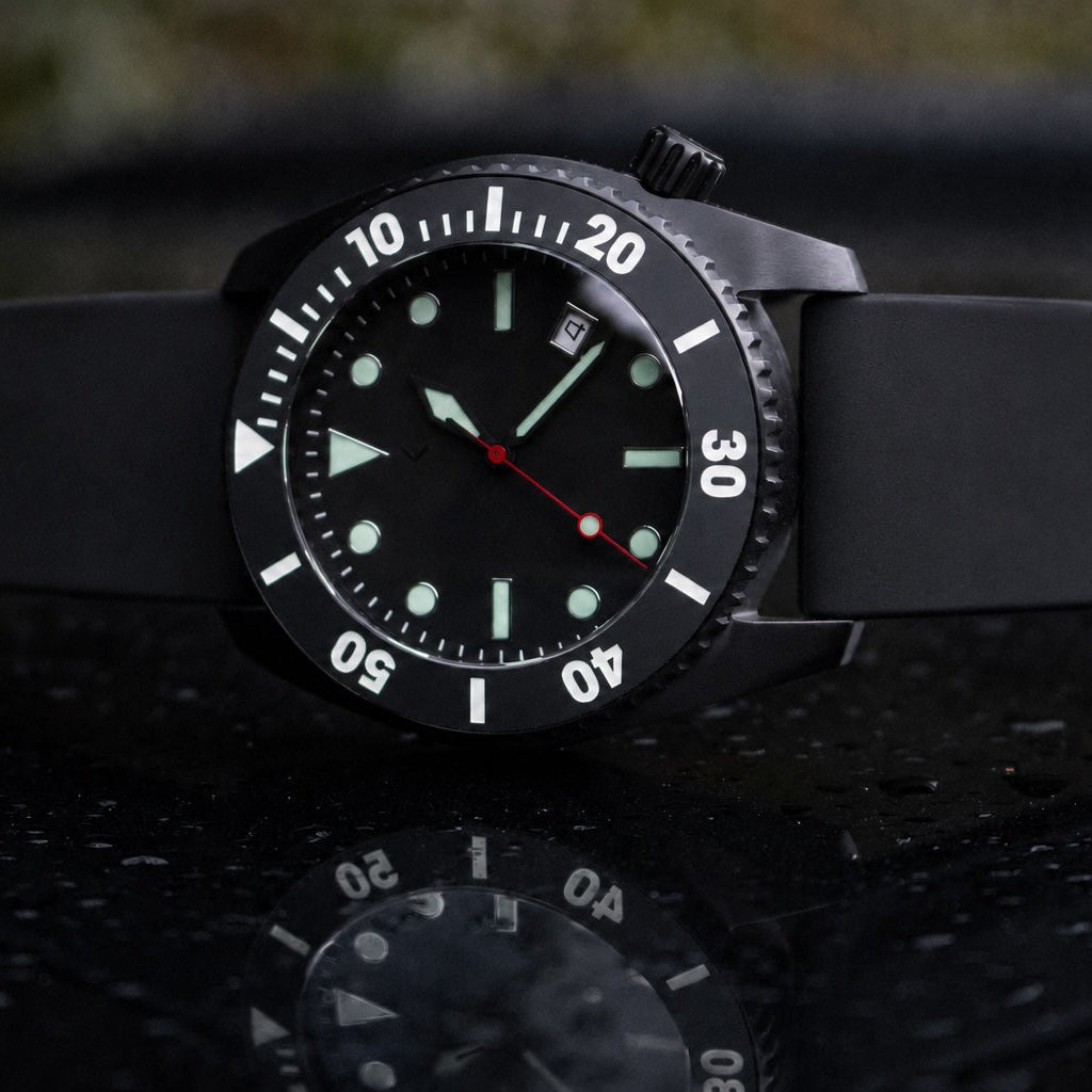 A black analog dive watch with a black silicone strap, featuring a black dial with luminous indices, a white rotating bezel, and red accent hands.