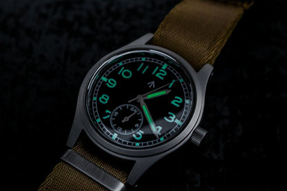 Close-up of the black dial of the Aeschbach x Enoksen 'Fly' E03/H watch in darkness, showing the Super-Luminova effect and legibility.