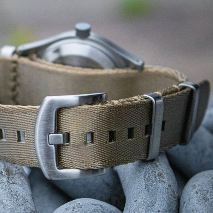 The Aeschbach x Enoksen 'Fly' E03/T watch displayed with a khaki seatbelt NATO strap.
