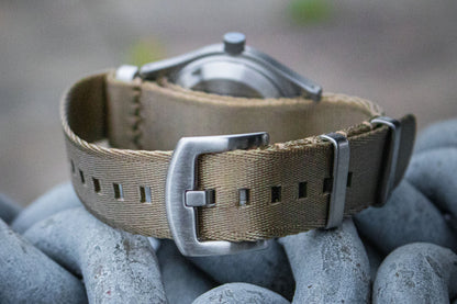 The Aeschbach x Enoksen 'Fly' E03/H watch displayed with a khaki seatbelt NATO strap.