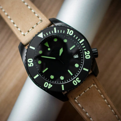 Watch with a black dial and green hour markers on a brown leather strap.
