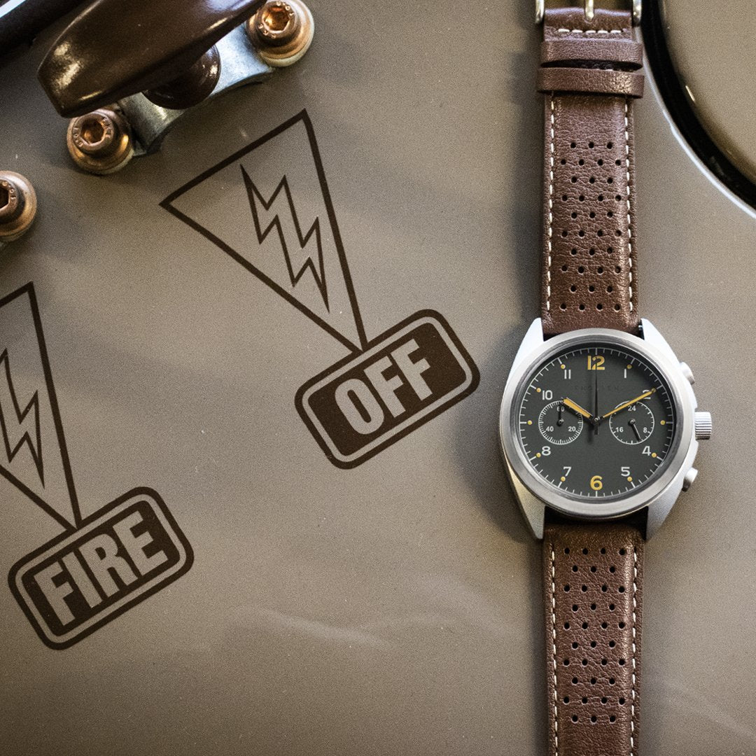 Watch with brown leather strap on a surface with 'OFF' and 'FIRE' labels.