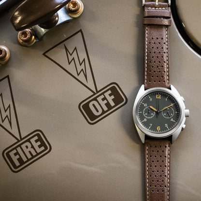 Watch with brown leather strap on a surface with 'OFF' and 'FIRE' labels.