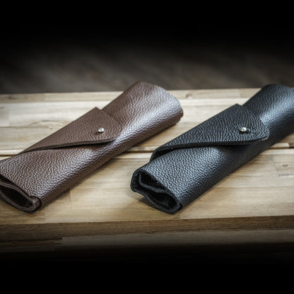 Two leather pouches, one brown and one black, on a wooden surface with a dark background.