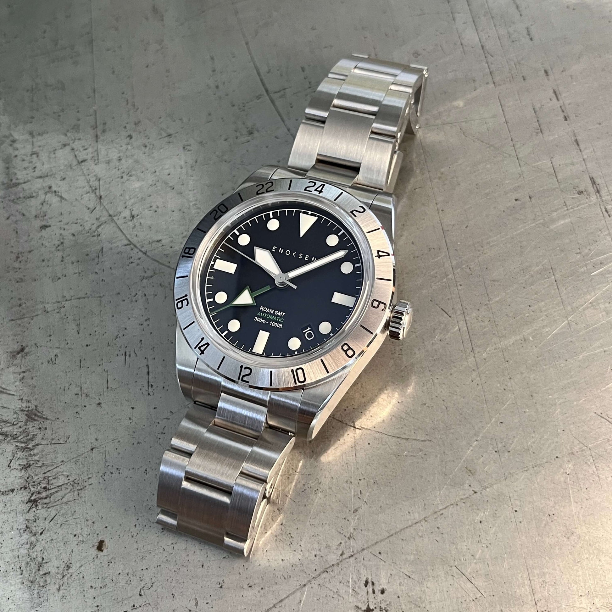 GMT watch, close-up. Emphasizes the quality of the watch and clearly shows the green GMT hand set against the black dial, providing a classic appearance.