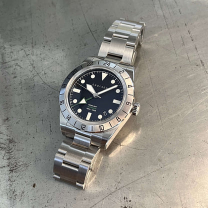 GMT watch, close-up. Emphasizes the quality of the watch and clearly shows the green GMT hand set against the black dial, providing a classic appearance.