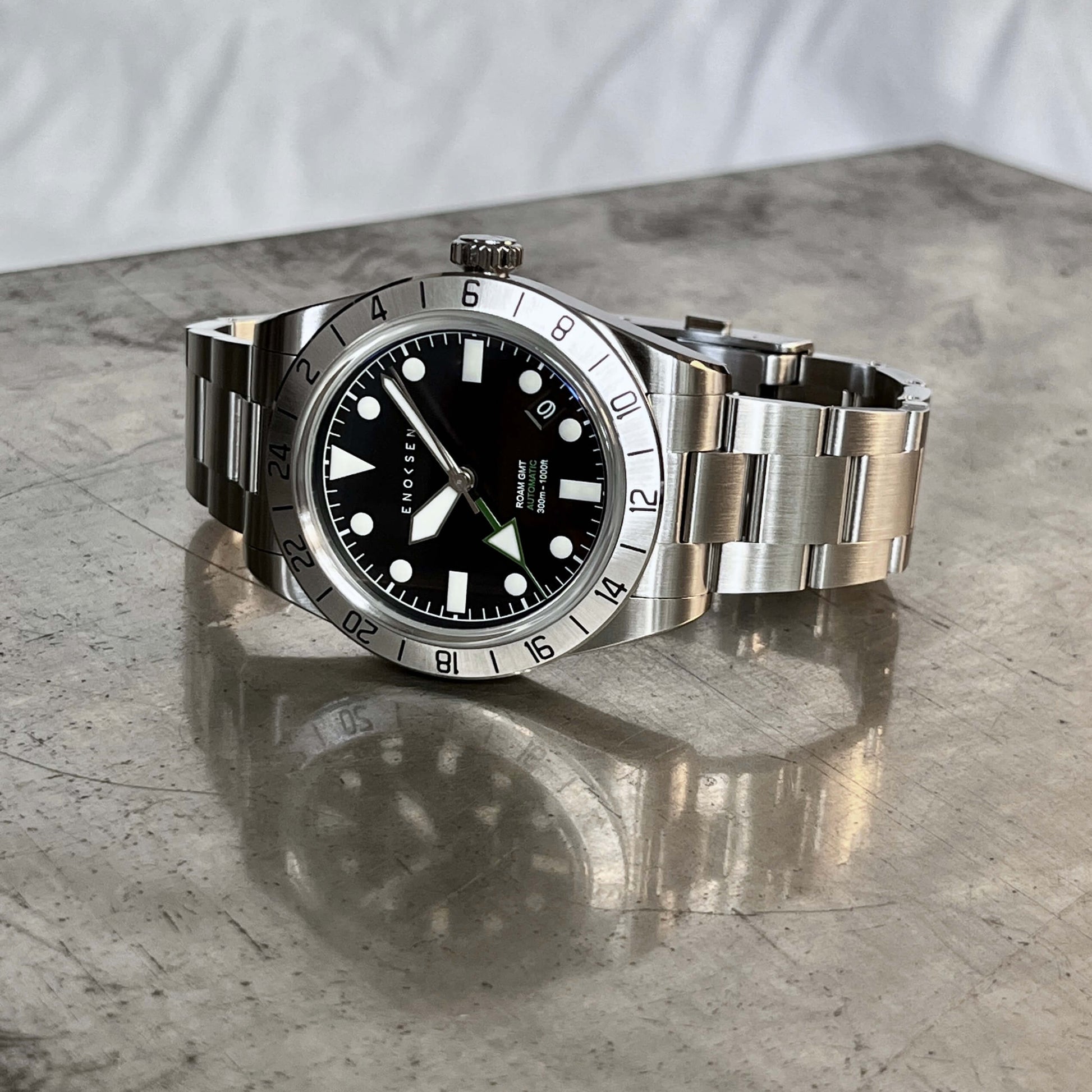 Roam E07/B men's automatic GMT By Enoksen watch featuring a polished stainless steel link bracelet, front view. The image emphasizes the anti-reflective, scratch-resistant sapphire Crystal.