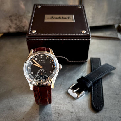 The Aeschbach 1944 swiss watch presented in a gift box on a brown leather crocodile-style strap, shown with one included additional strap: a black leather strap.