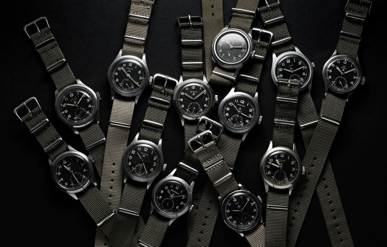 Dirty Dozen watches. The twelve original watches are laid out on a black background. With army green nato straps.