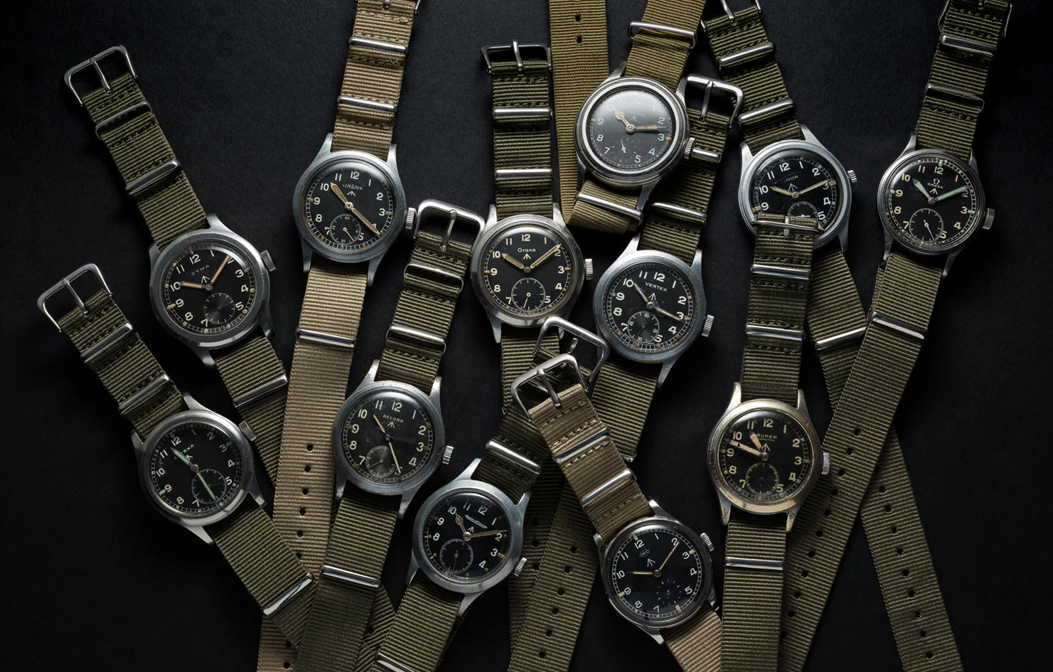 Dirty Dozen watches. The twelve original watches are laid out on a black background. With army green nato straps.