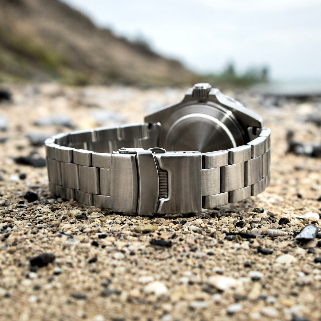 Steel diver's watch with metal bracelet on a rocky surface. Screw-in caseback is visible.