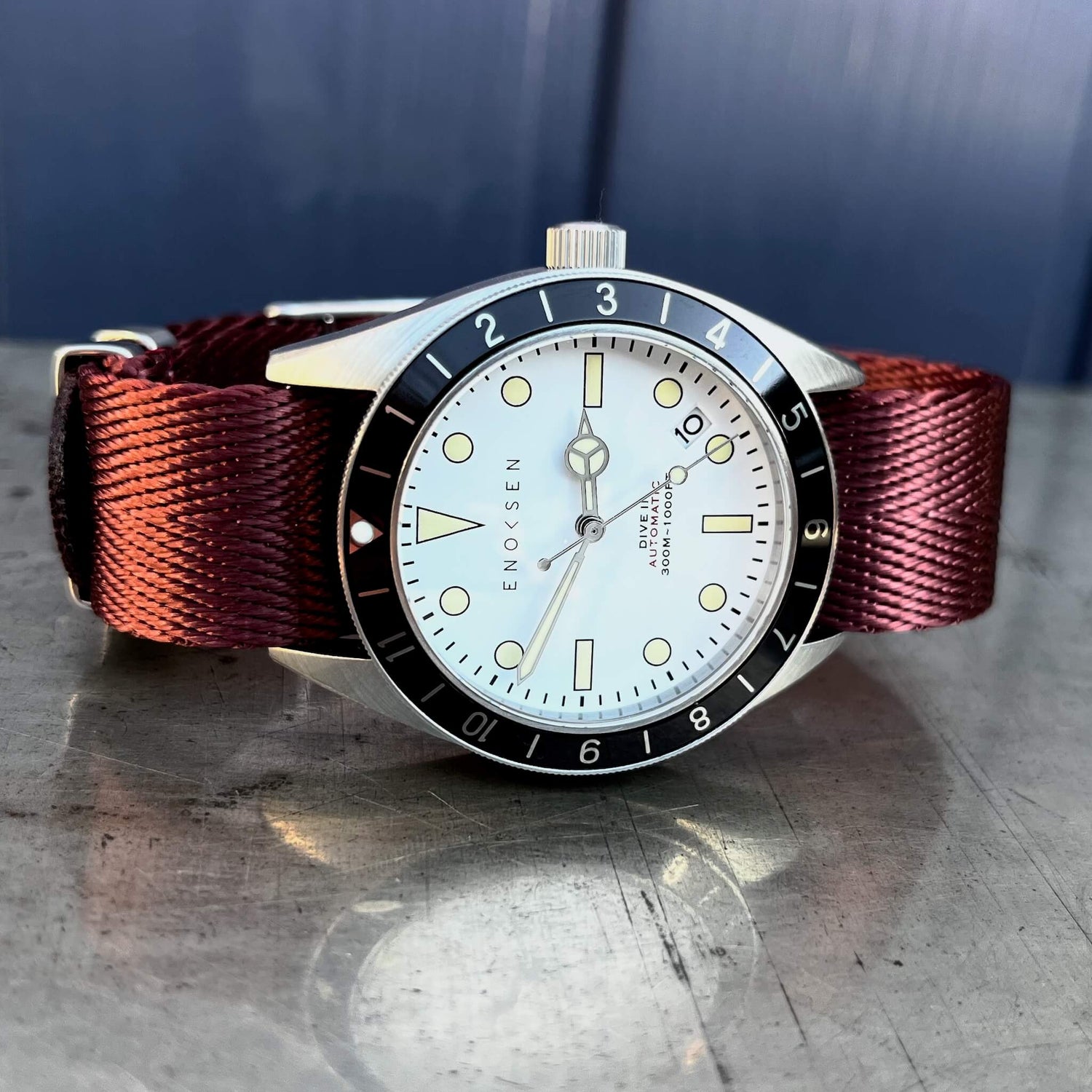 Dive II with white dial on burgundy herringbone woven strap, angled wrist-ready view.