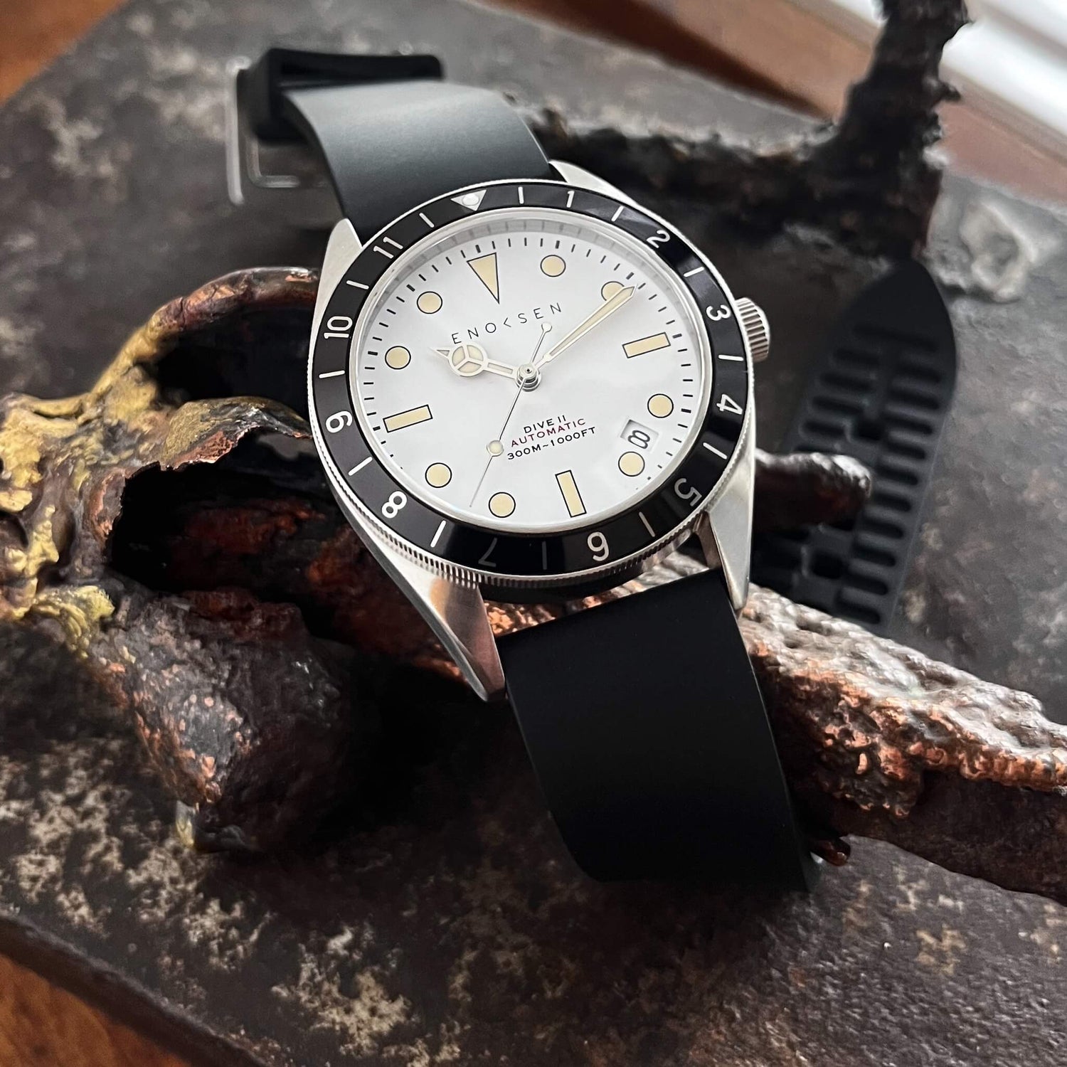 Dive II with white dial photographed on a bronze sculpture, showing the classic skin-diver silhouette.