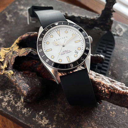 Dive II with white dial photographed on a bronze sculpture, showing the classic skin-diver silhouette.