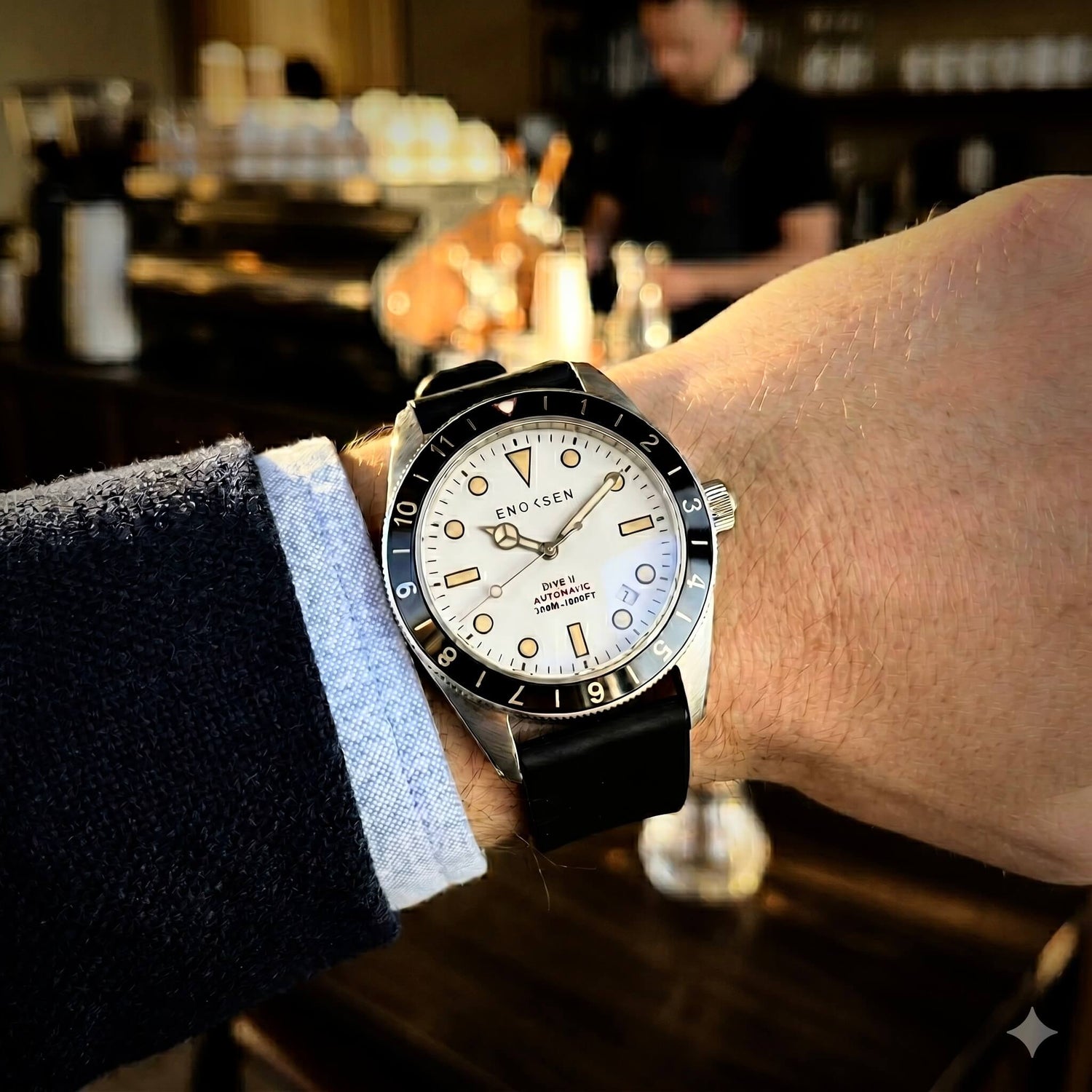 Enoksen Dive II E12/A white dial worn on a wrist size 18cm, showcasing the proportions of the watch and the classic skin-diver profile. Background is  a coffee shop.