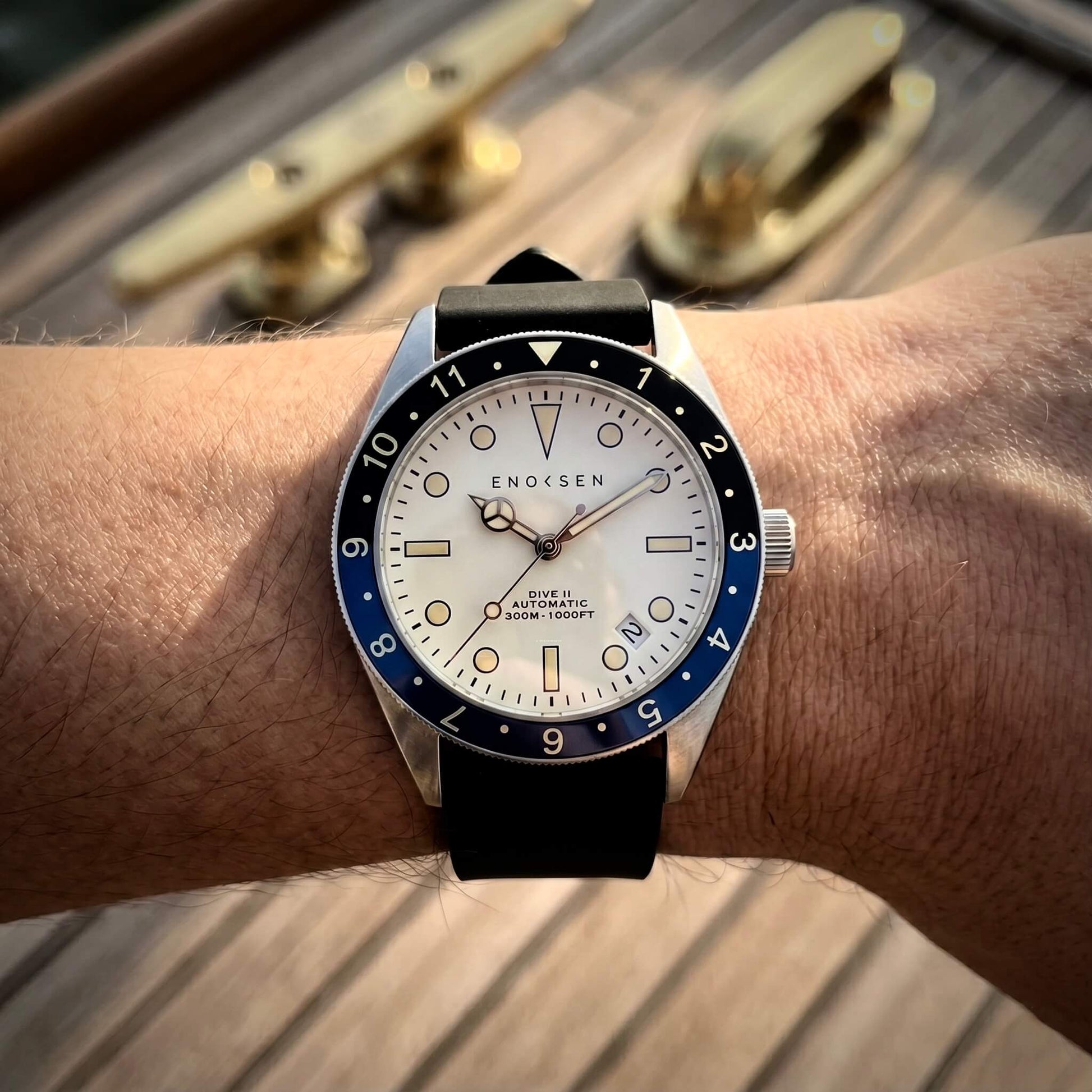Enoksen Dive II E12/A white dial worn on a wrist size 19cm, showcasing the proportions of the watch and the classic skin-diver profile. Background is on a sunny boat deck.