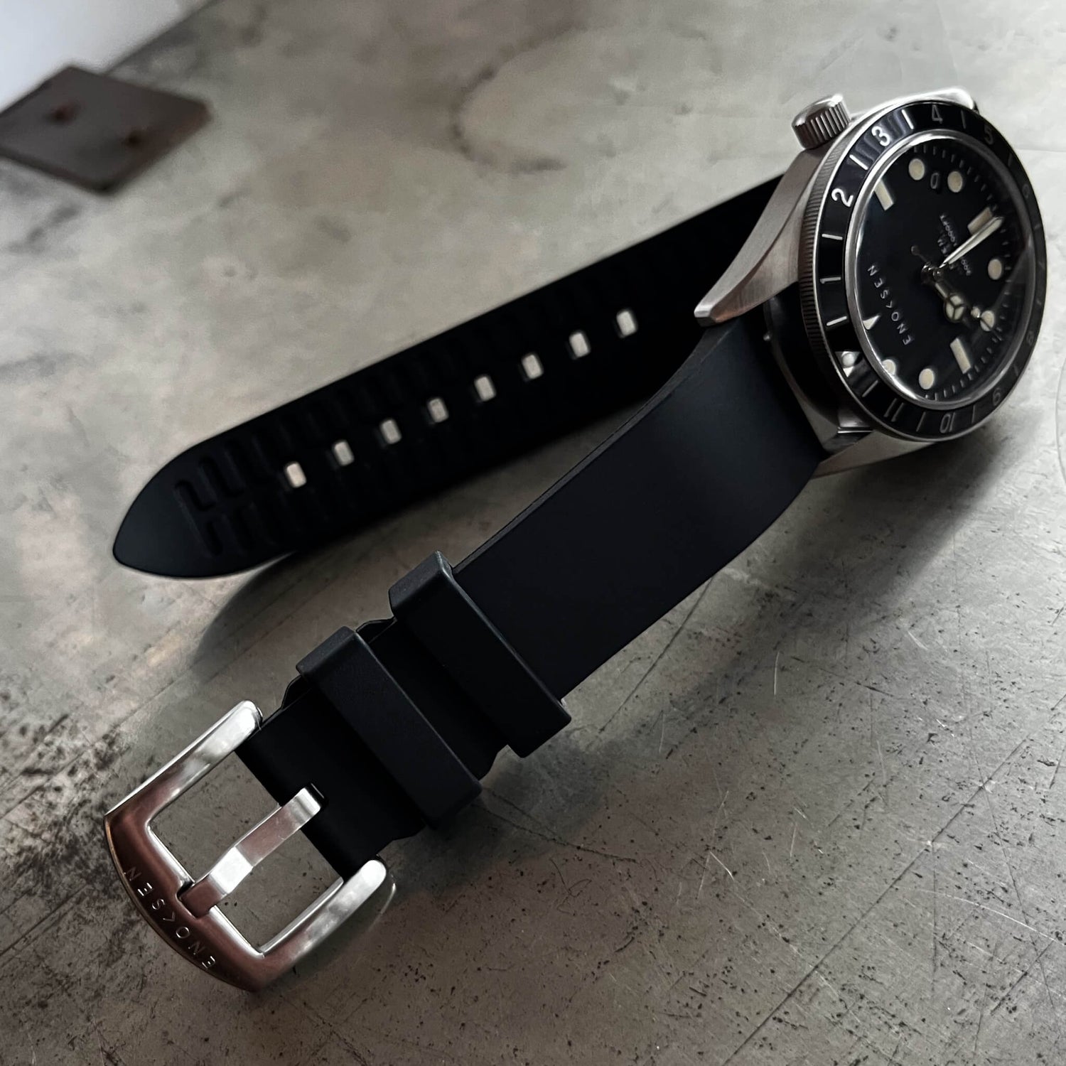 Black natural rubber strap with brushed steel buckle and Enoksen logo engraving.