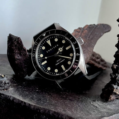 Dive II with black dial photographed with a bronze sculpture, showing the classic skin-diver silhouette.