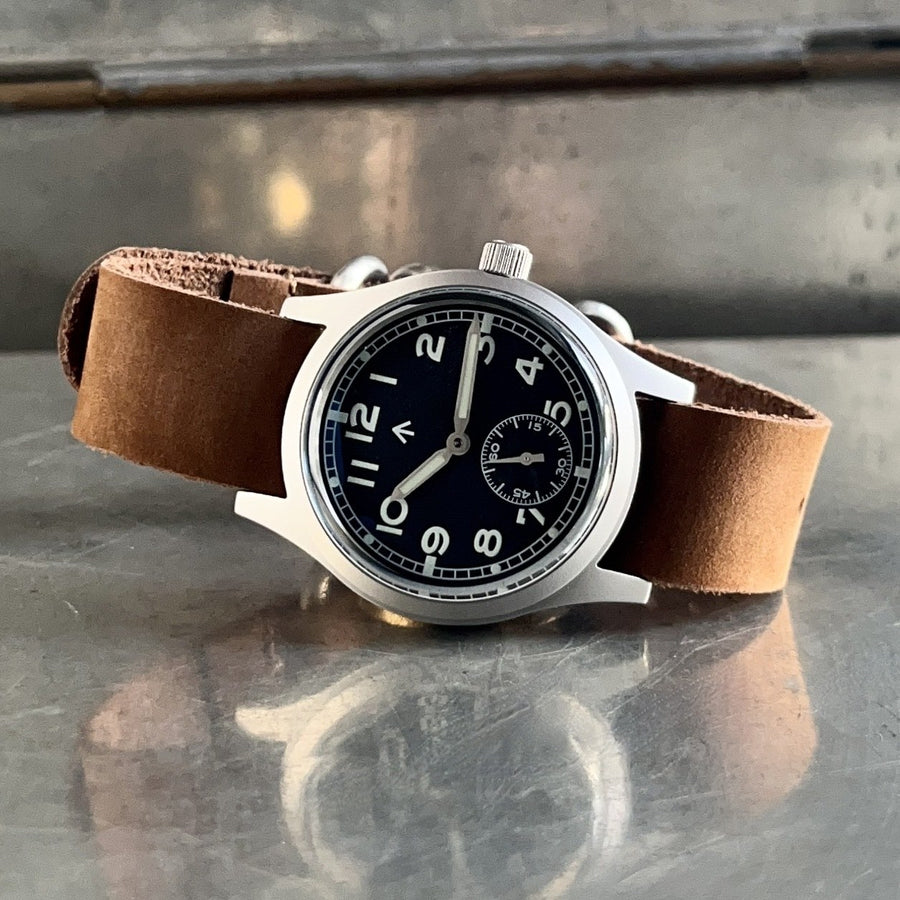 Enoksen fly E03/M black dial Dirty Dozen watch on a brown suede strap on distressed metal box with reflection.