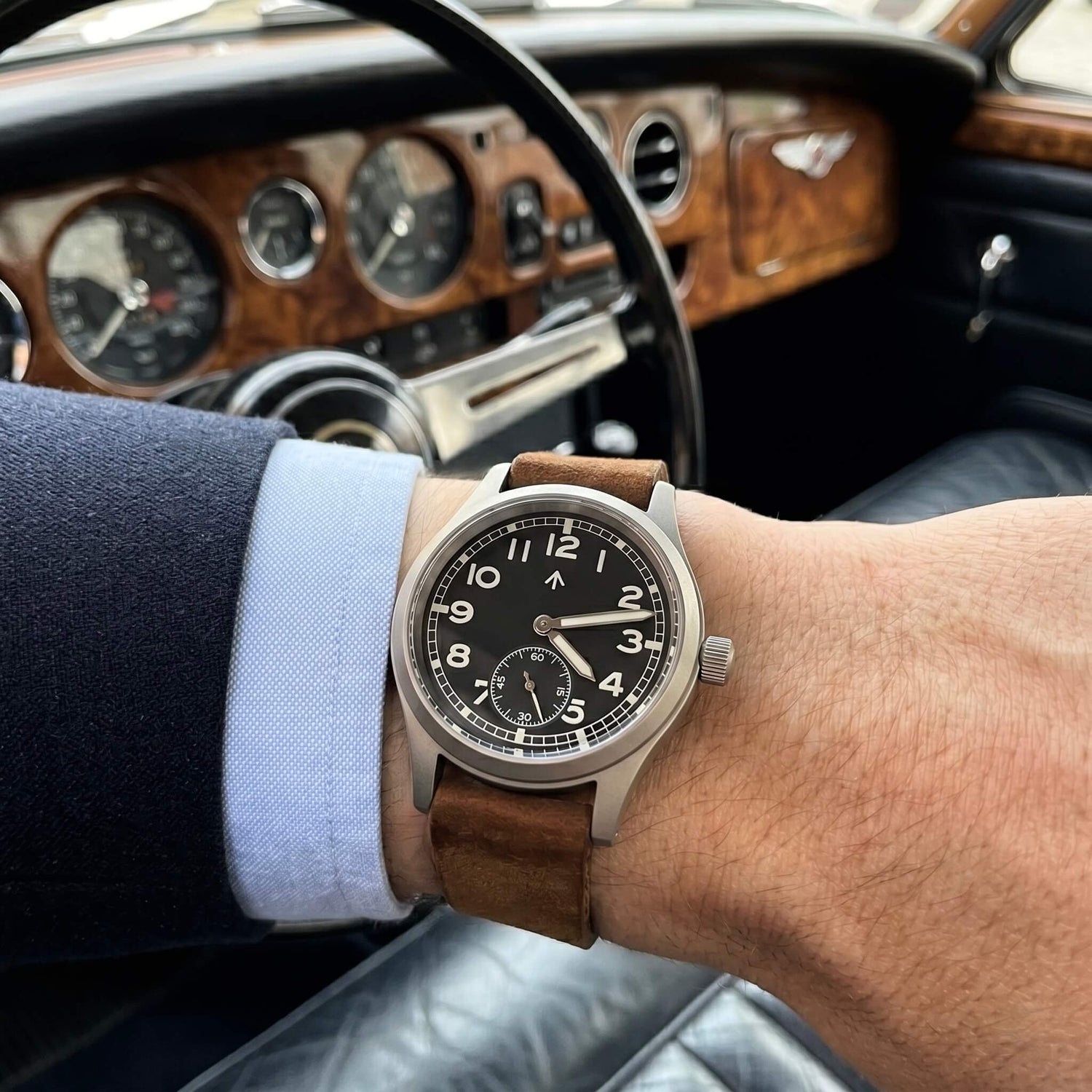 Enoksen Fly E03 M Swiss 36mm watch with black dial worn on a wrist size 18cm, showcasing the proportions and military case shape make it wear slightly larger than the numbers suggest. Classic car as background.