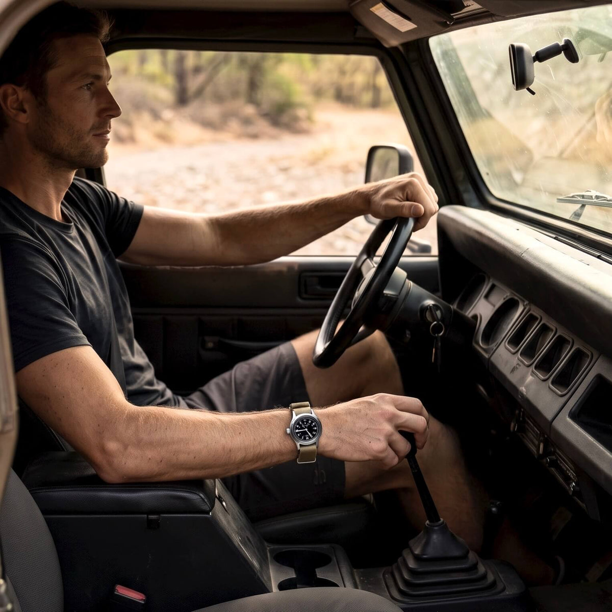Enoksen Fly E03/S watch with a black dial and khaki NATO strap worn on a wrist by a man sitting in a Jeep.