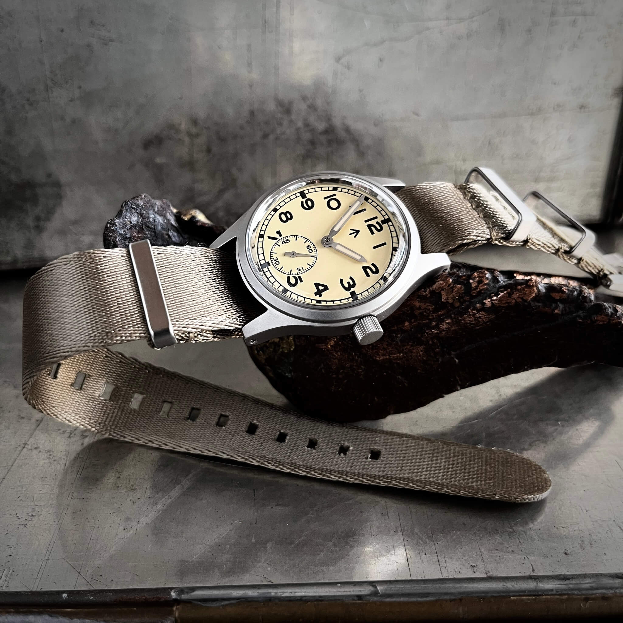 Fly E03/T cream dial with khaki NATO double pass strap photographed on a bronze sculpture, showing the classic domed profile of the glass.