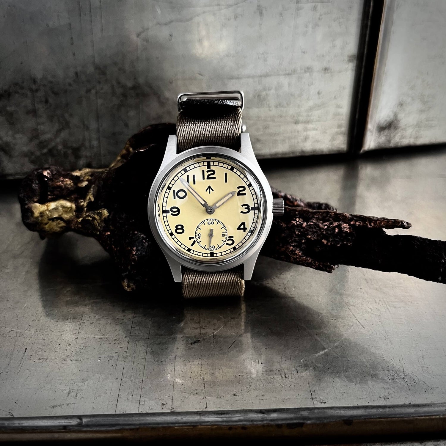 Fly E03/T cream dial with khaki NATO double pass strap photographed on a bronze sculpture, showing the classic Dirty Dozen dial.